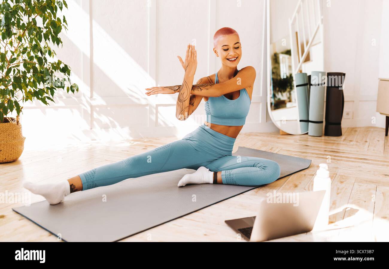 Praticienne de yoga s'étirant dans une pièce lumineuse avec un ordinateur portable le matin Banque D'Images