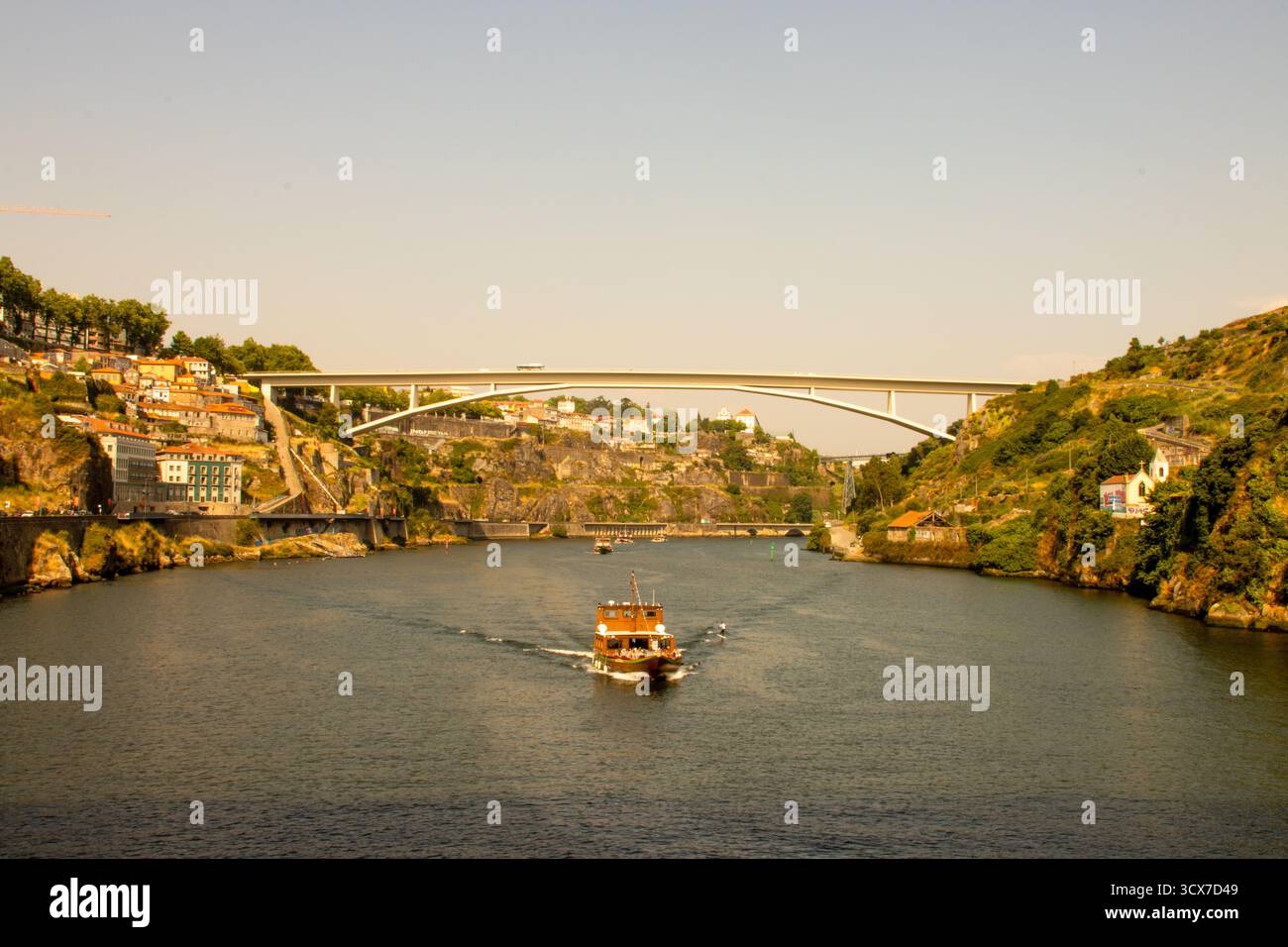 Bateau d'excursion naviguant sur le fleuve Douro sous le pont Arrábida à Porto, Portugal, par un après-midi ensoleillé avec vue sur la ville et lumière dorée. Banque D'Images