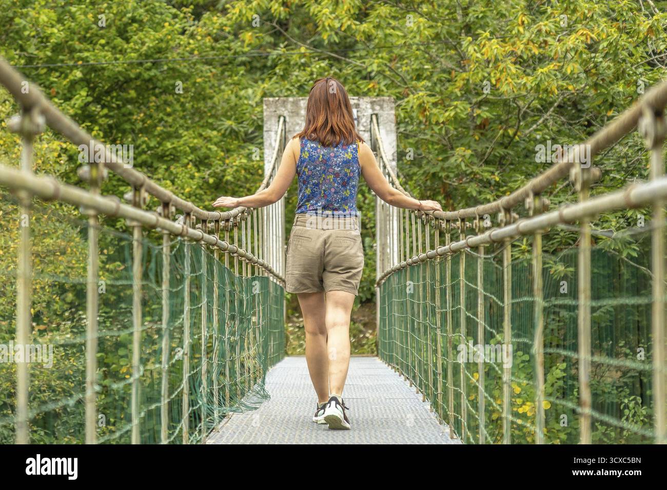Touriste jouissant d'une promenade paisible à travers un pont suspendu métallique, entouré d'une végétation luxuriante, sur la route de la rivière Dobra à th Banque D'Images
