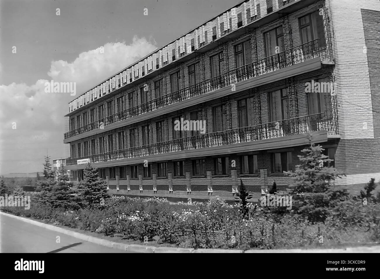 Une photo d'archives des années 1980 capture le sanatorium-prophylactorium 'Khimik' à Sloviansk, en RSS d'Ukraine. Ce bâtiment en briques de quatre étages, avec ses longues rangées de balcons, a servi de centre de santé pour les travailleurs de l'usine chimique voisine. Le panneau 'Dobro Pozhalovat !' (Bienvenue !) accueille les visiteurs à l'entrée. Les terrains bien entretenus avec de jeunes sapins et des parterres de fleurs reflètent l'accent soviétique sur le bien-être des travailleurs. Cette image est un enregistrement unique de l'infrastructure sociale dans un Donbass pacifique avant la guerre Banque D'Images