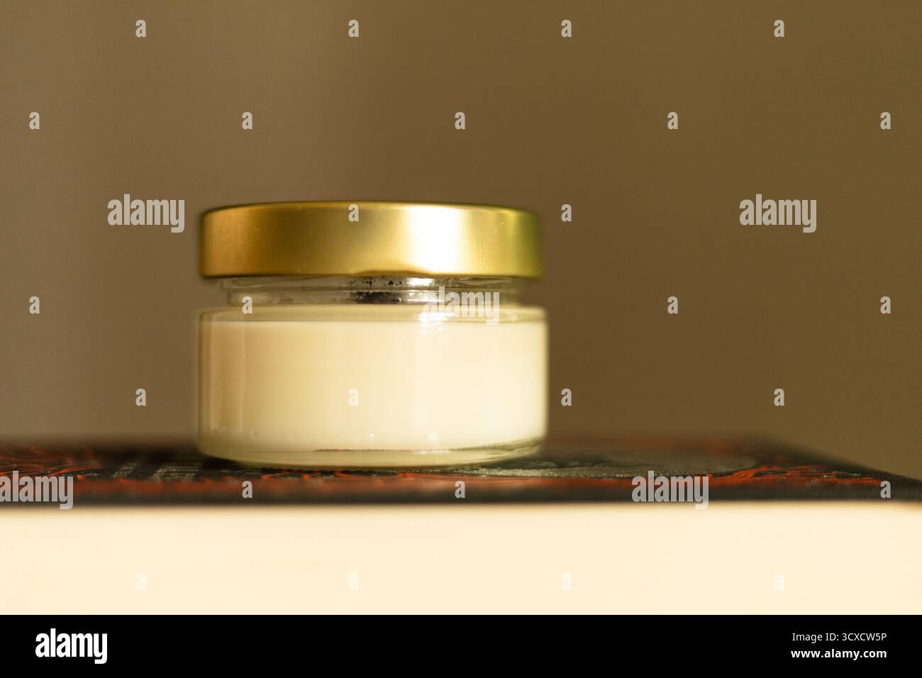 Bougie de soja minimaliste dans un pot en verre placé sur des livres. Composition chaleureuse et calme parfaite pour la détente, la décoration intérieure et les thèmes de l'auto-soin Banque D'Images