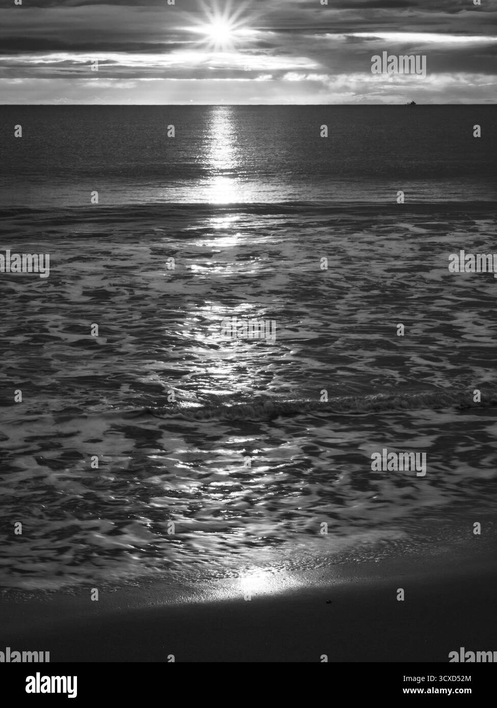Reflet du lever du soleil sur la mer et le sable humide avec bateau lointain en noir et blanc Banque D'Images