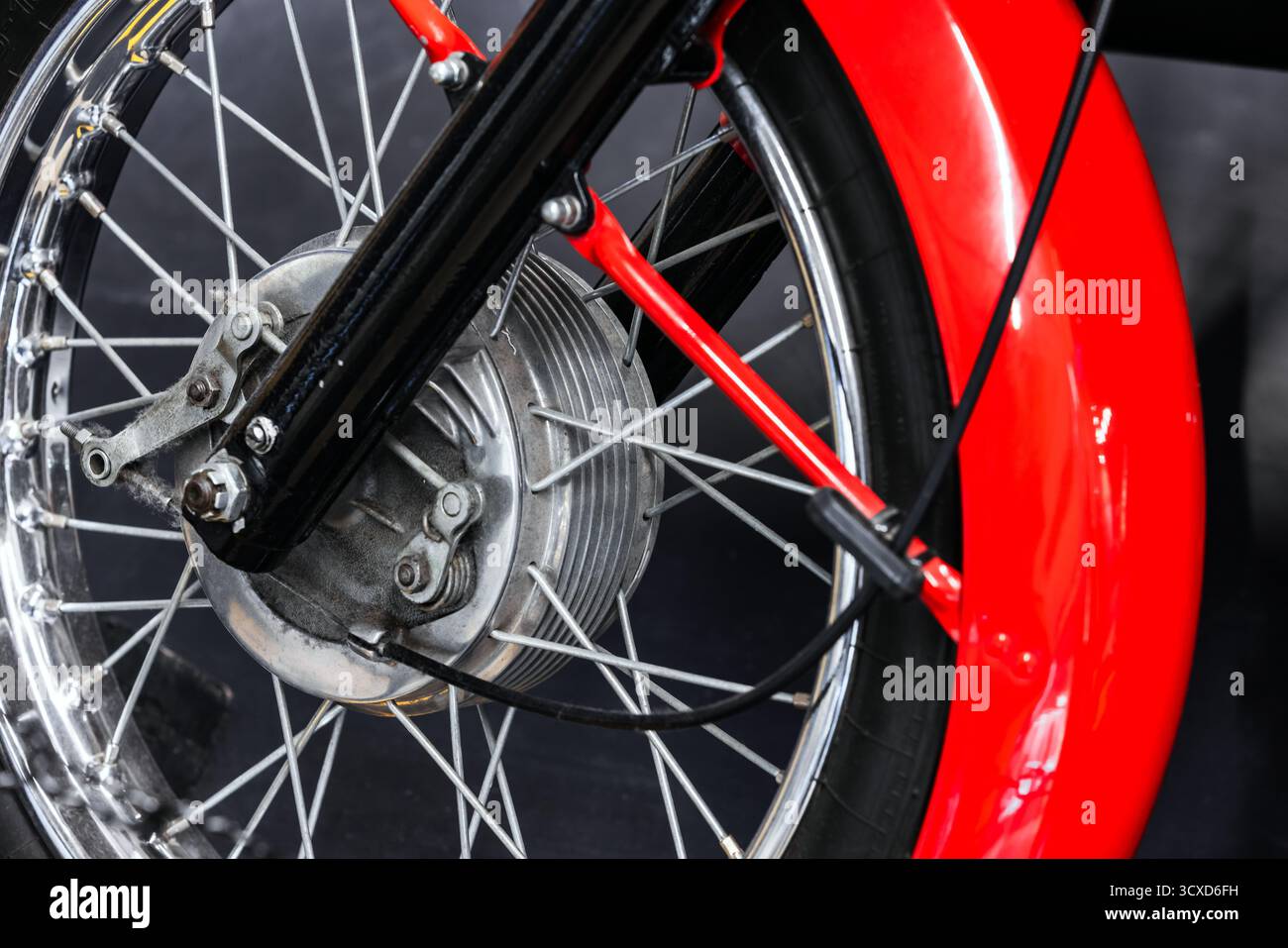 Gros plan détaillé d'une roue avant de moto vintage avec un frein à tambour argenté, des rayons fins et un garde-boue rouge brillant. Idéal pour l'automobile, mac Banque D'Images