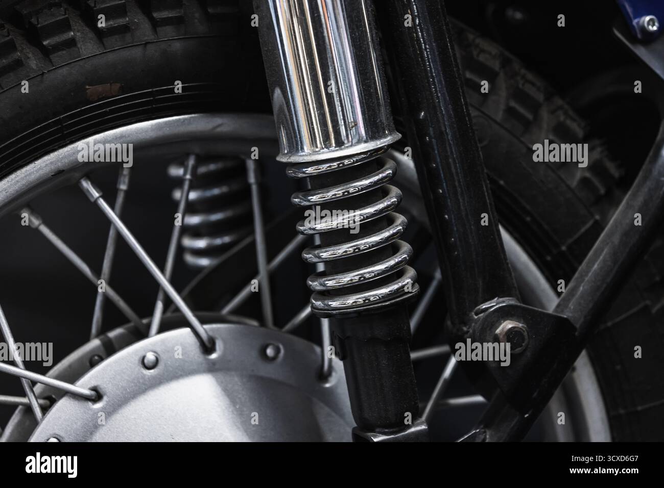 Gros plan détaillé d'une suspension avant de moto avec ressort hélicoïdal chromé, fourche et roue à rayons. Les textures métalliques robustes véhiculent Mechan Banque D'Images