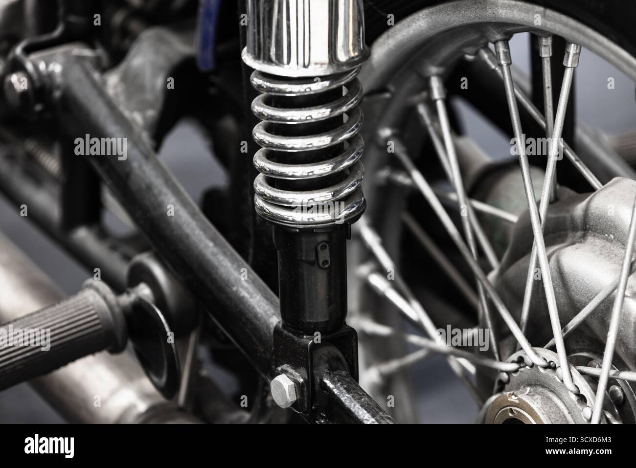 Photo en gros plan d'une suspension de moto avec un ressort hélicoïdal chromé, une fourche et une roue à rayons. Les textures métalliques robustes transmettent la précision mécanique Banque D'Images