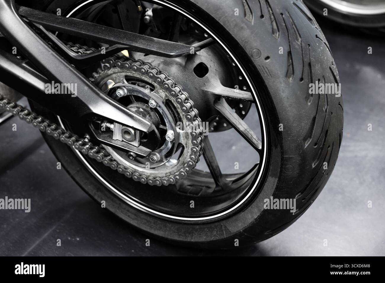Un gros plan détaillé d'une roue arrière de moto, chaîne, pignon et pneu. Les composants métalliques contrastent avec le caoutchouc foncé, mettant en évidence d mécanique Banque D'Images