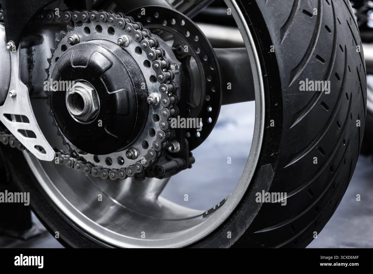 Roue arrière, chaîne, roue dentée et pneu de motocyclette. Les composants métalliques contrastent avec le caoutchouc foncé, soulignant la conception mécanique et le vélo sport A. Banque D'Images