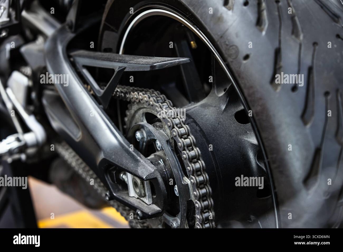 Photographie rapprochée d'une roue arrière, d'une chaîne, d'un pignon et d'un pneu de moto. Les composants métalliques contrastent avec le caoutchouc foncé, mettant en évidence la mécanique Banque D'Images