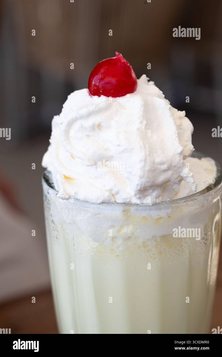 Un milk-shake délicieux et crémeux garni de crème fouettée moelleuse et d'une cerise brillante, idéal pour les chaudes journées d'été Banque D'Images