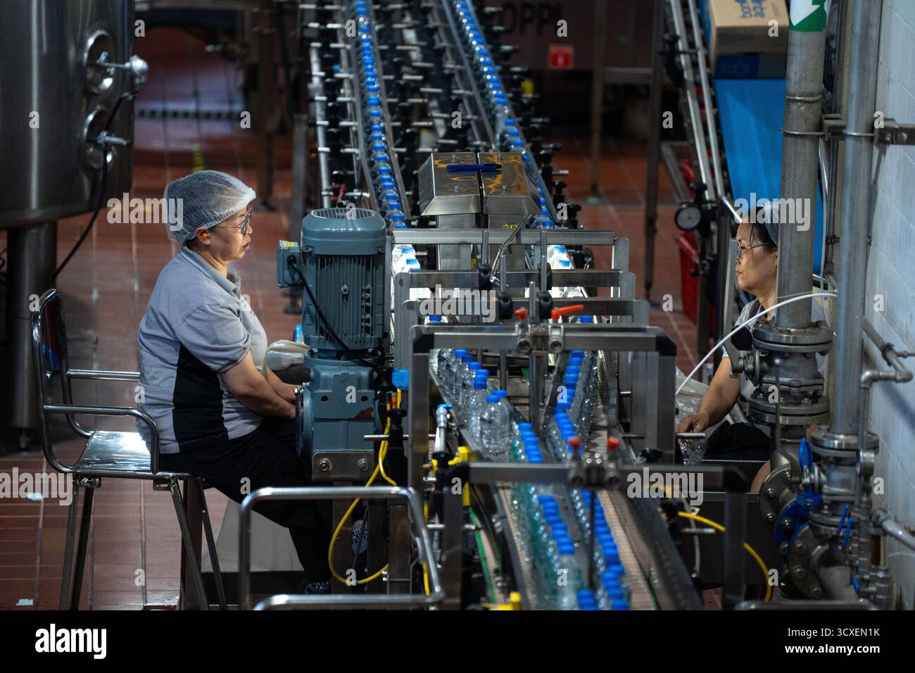 Deux travailleurs inspectent des bouteilles d'eau bonaqua sur la chaîne de production de l'usine d'embouteillage Swire Coca-Cola le 14 octobre 2025 à Hong Kong. (Photo de Vernon Yuen/Nexpher images) Banque D'Images