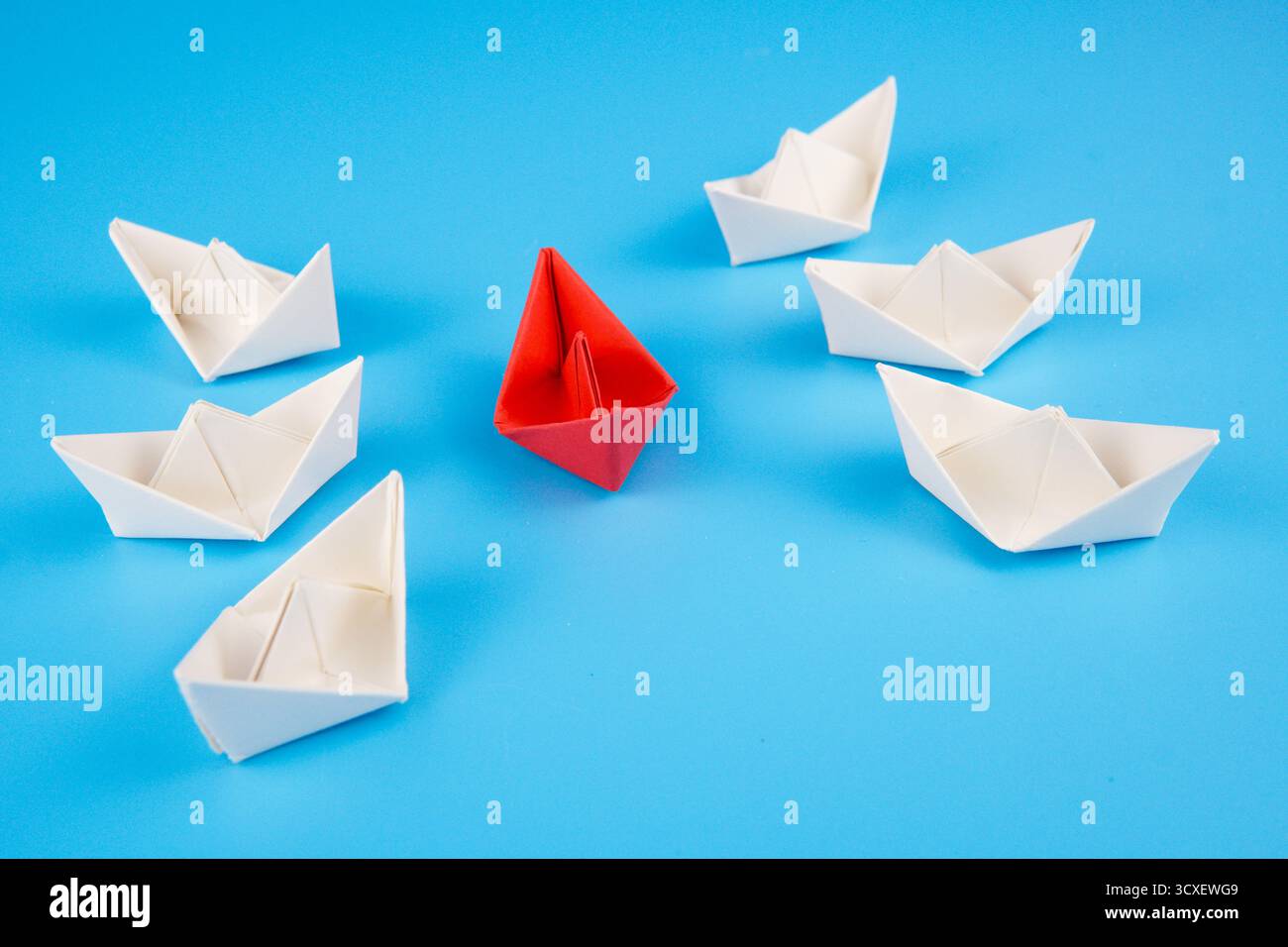 Photo symbolique montrant un bateau de papier rouge entouré de bateaux blancs sur fond bleu, représentant un navire d'aide humanitaire entouré. Banque D'Images