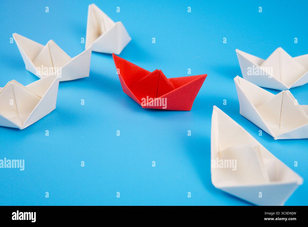 Photo symbolique montrant un bateau de papier rouge entouré de bateaux blancs sur fond bleu, représentant un navire d'aide humanitaire entouré. Banque D'Images