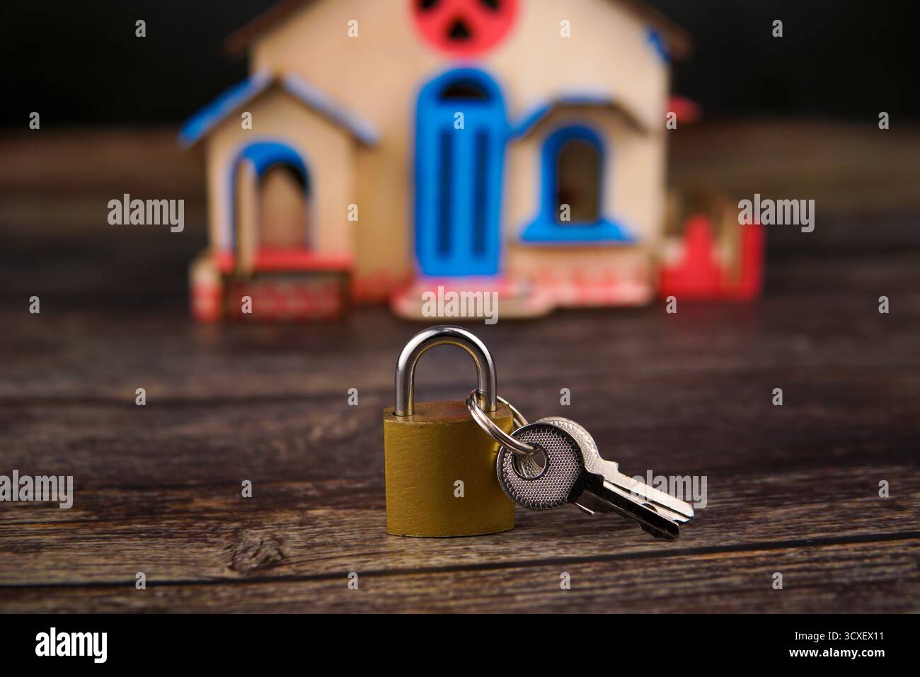 Cadenas et clés placés devant un petit modèle de maison en bois sur une table en bois foncé, représentant la protection de la propriété, hypothèque. Banque D'Images