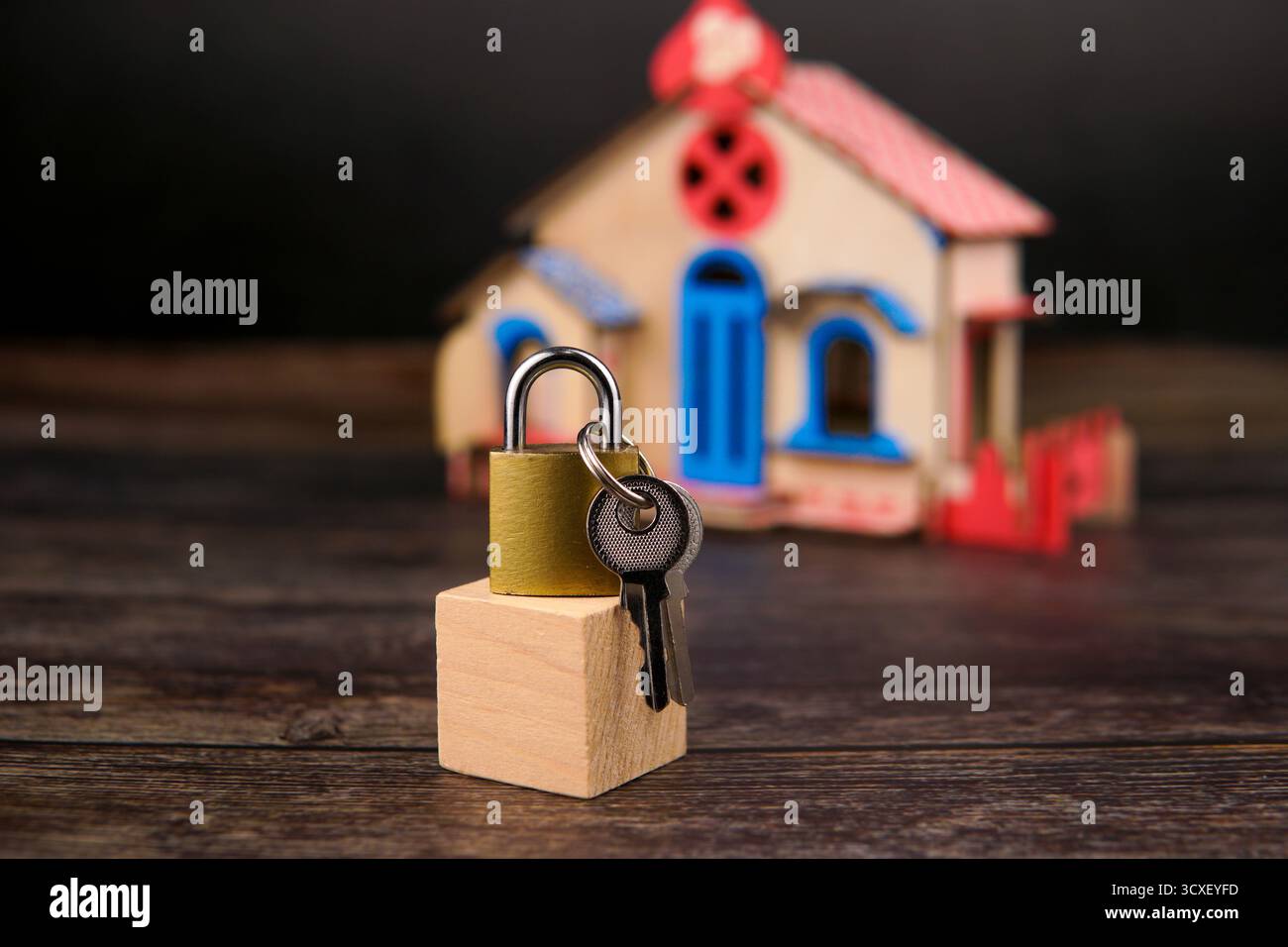 Cadenas et clés placés sur un bloc de bois devant une maison miniature floue, représentant la propriété, la sécurité financière, l'investissement immobilier. Banque D'Images