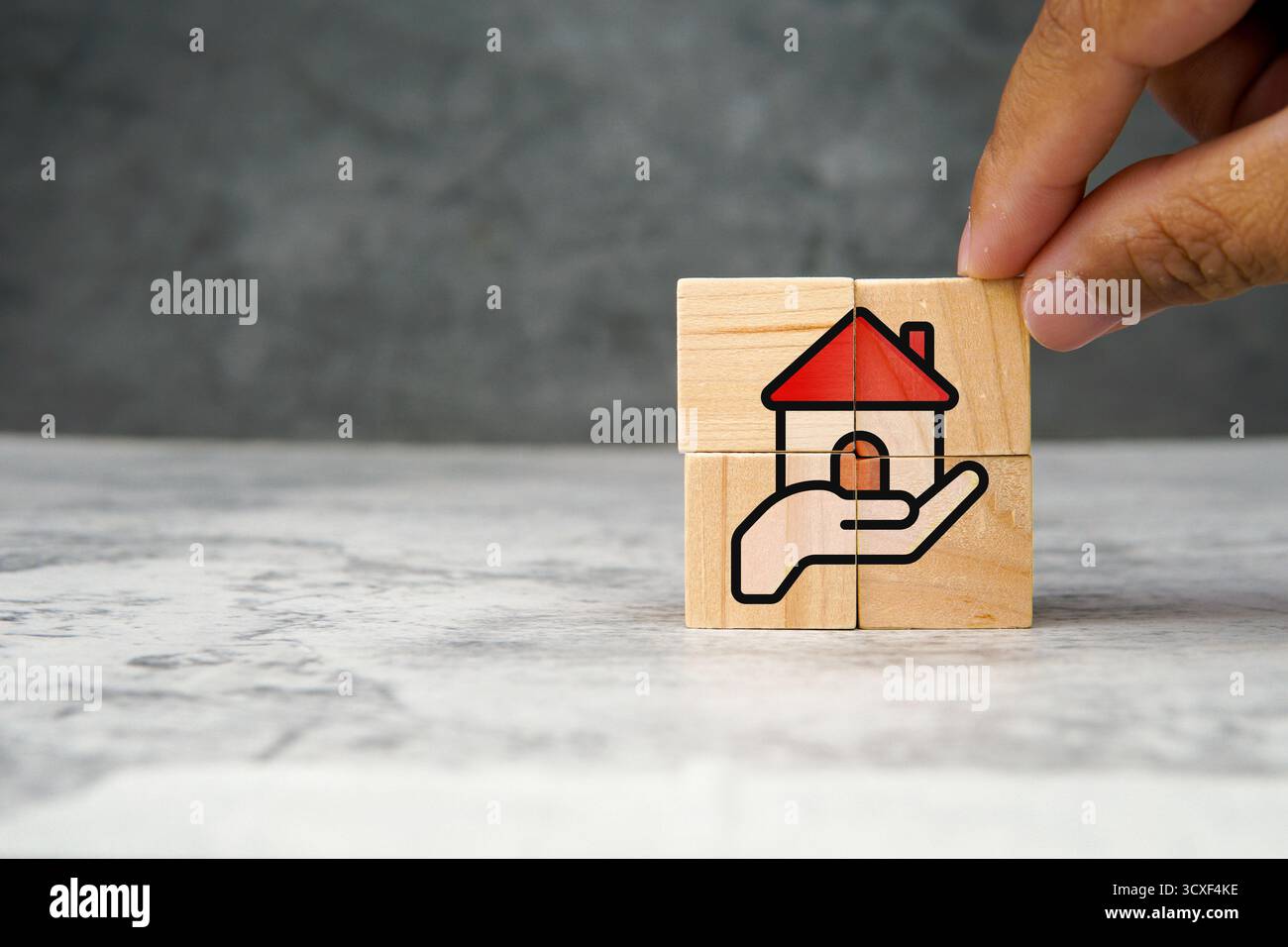 Cubes en bois avec illustration d'une maison au toit rouge reposant sur une main, symbolisant l'assurance de biens, l'investissement immobilier, l'hypothèque ou les soins immobiliers. Banque D'Images