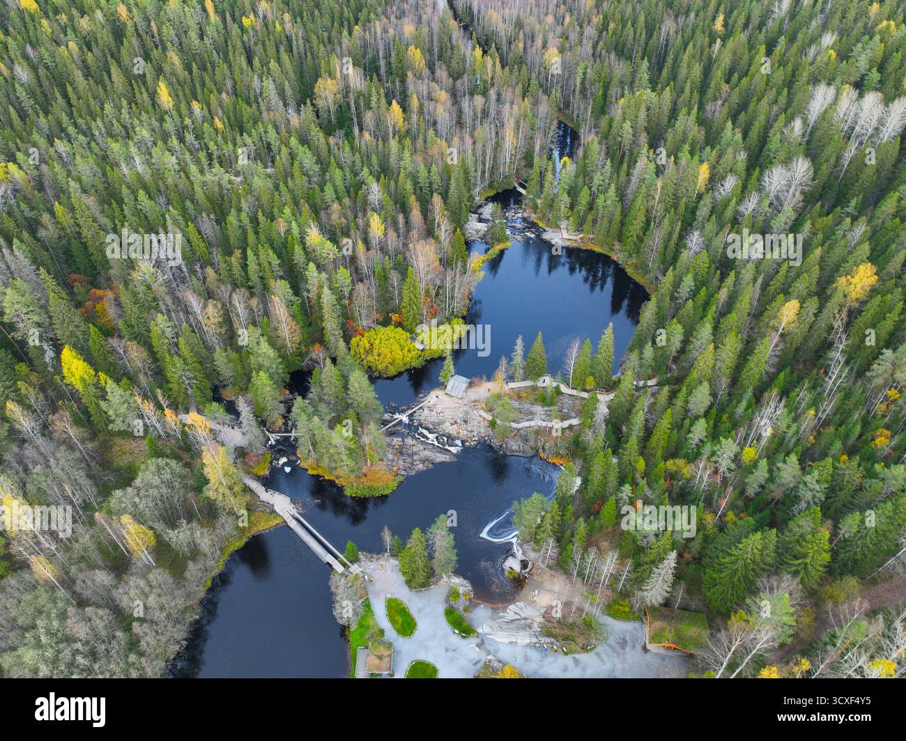 Vue en angle élevé sur la forêt luxuriante et le feuillage jaune d'automne entourant un lac sombre et immobile avec un pont en bois et une petite infrastructure touristique Banque D'Images