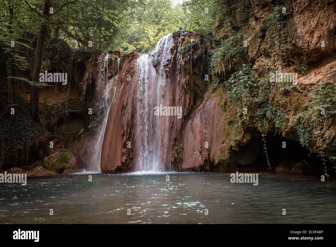 Une cascade au milieu d'une forêt, en cascade dans un petit lac peu profond, entouré de rochers couverts de lierre et d'une végétation luxuriante. Banque D'Images