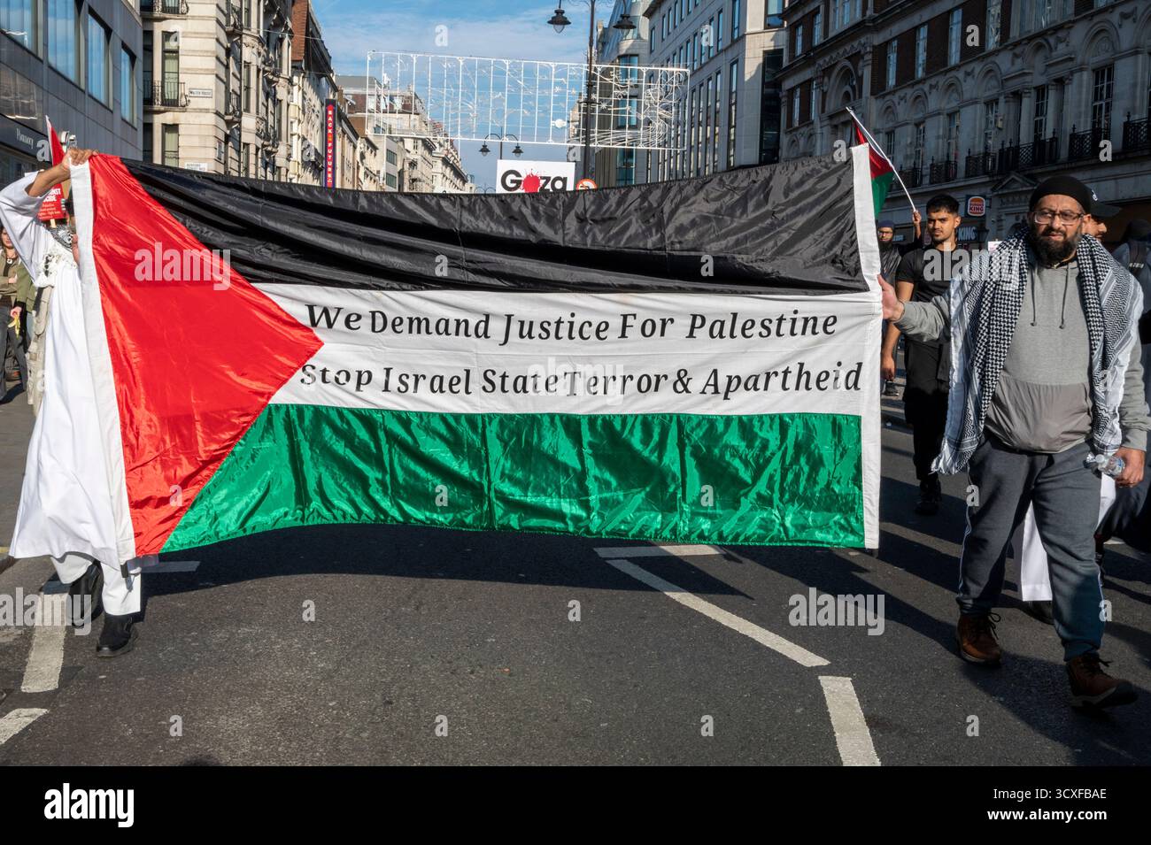Manifestation nationale pour la Palestine, Londres. Les manifestants portent un grand drapeau palestinien avec « nous exigeons justice pour la Palestine, arrêtons la terreur d'État » Banque D'Images
