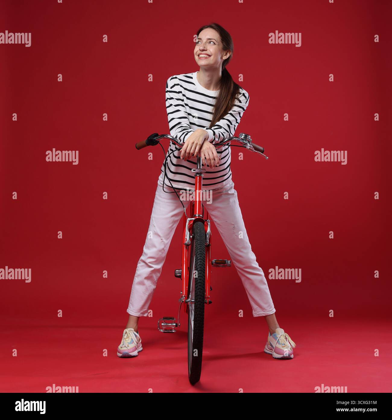 Femme souriante posant sur le vélo sur fond rouge Banque D'Images