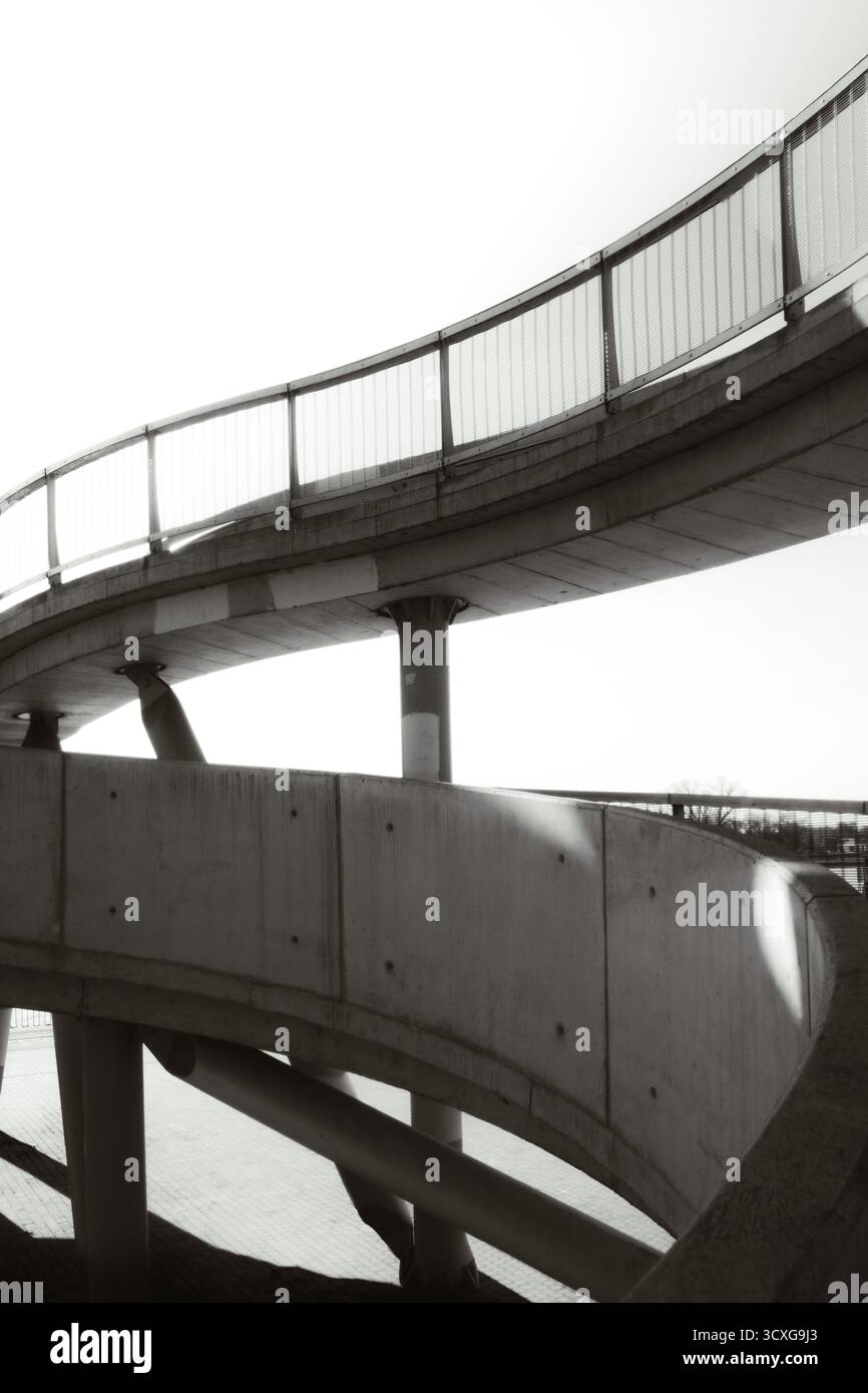 Détail architectural moderne d'un pont piétonnier courbe capturé en noir et blanc, mettant l'accent sur la géométrie, les lignes et le minimalisme Banque D'Images