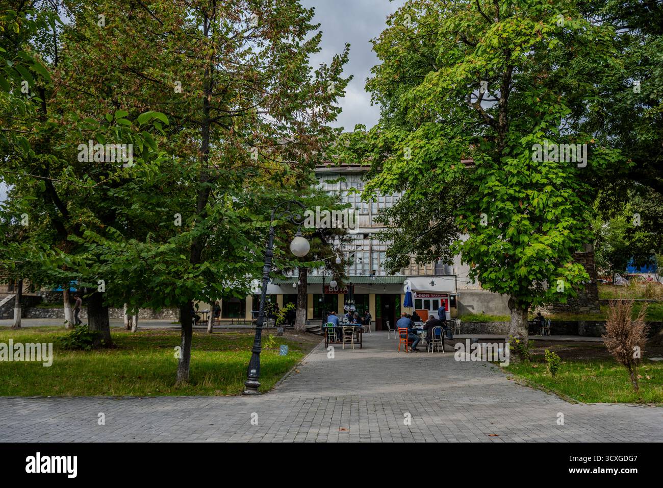 Personnes assises dans un café en plein air entouré d’arbres verts dans un parc de Shaki, Azerbaïdjan – 22 septembre 2025. Banque D'Images