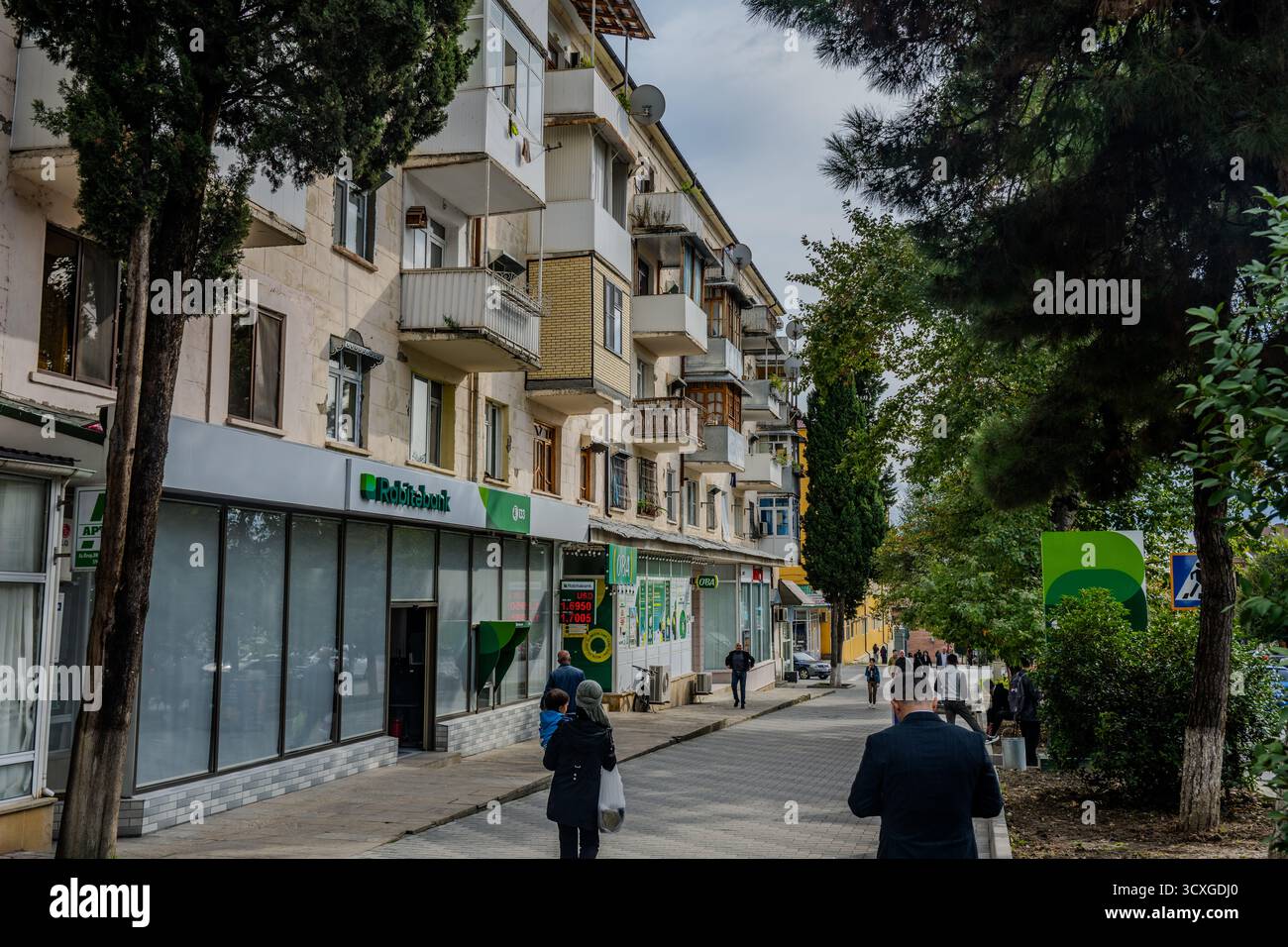 Des gens marchant le long d’une rue commerçante bordée de banques et d’immeubles d’habitation à Shaki, Azerbaïdjan – 22 septembre 2025. Banque D'Images