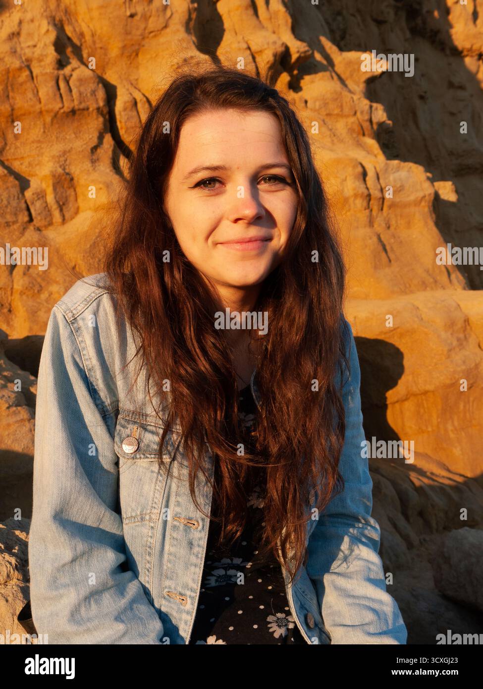 Jeune femme souriant à l'heure d'or contre des formations rocheuses côtières spectaculaires Banque D'Images