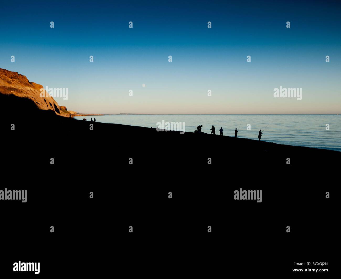 Silhouettes de personnes sur la plage au coucher du soleil avec des falaises dorées et une mer calme dans le Dorset Banque D'Images Silhouettes de personnes sur la plage au coucher du soleil avec des falaises dorées et une mer calme dans le Dorset Banque D'Images