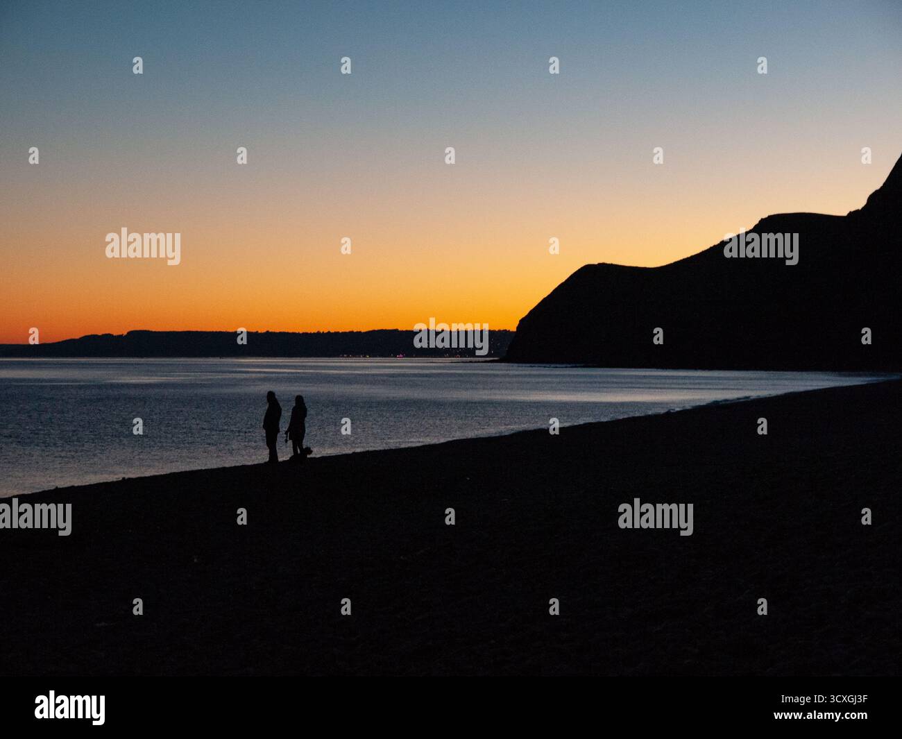 Deux silhouettes sur la plage au coucher du soleil avec un ciel orange spectaculaire et des falaises côtières Banque D'Images Deux silhouettes sur la plage au coucher du soleil avec un ciel orange spectaculaire et des falaises côtières Banque D'Images