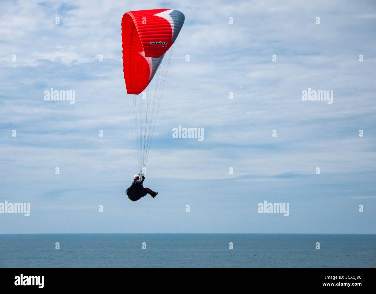 Parapente rouge planant au-dessus de la mer bleue et du ciel nuageux sur la côte du Dorset Banque D'Images