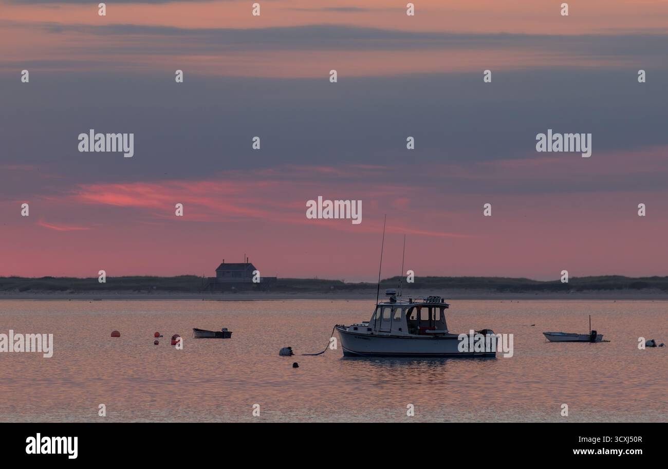 Bateau tranquille au coucher du soleil : un dory gris solitaire ancré dans l'eau calme, baigné de reflets chauds orange et rose. Paisible, serein et idyllique. Banque D'Images