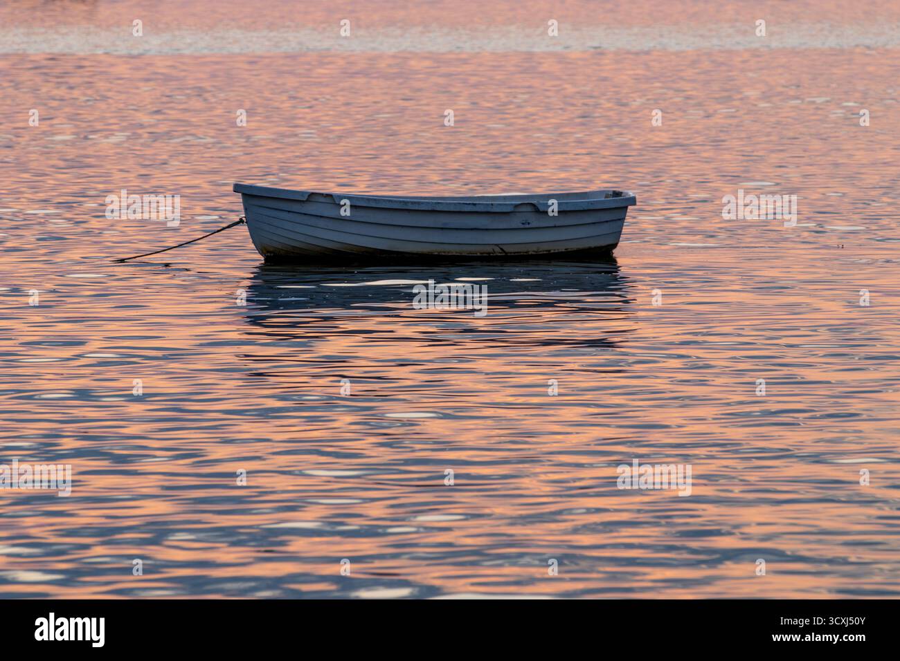 Bateau à rames tranquille au coucher du soleil : un dory gris solitaire ancré dans l'eau calme, baigné de reflets chauds orange et rose. Paisible, serein et idyllique. Banque D'Images