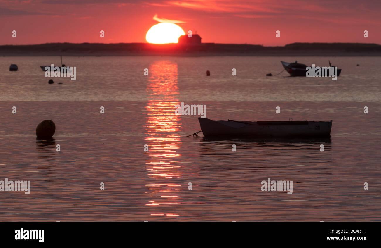 Bateau à rames tranquille au coucher du soleil : un dory gris solitaire ancré dans l'eau calme, baigné de reflets chauds orange et rose. Paisible, serein et idyllique. Banque D'Images