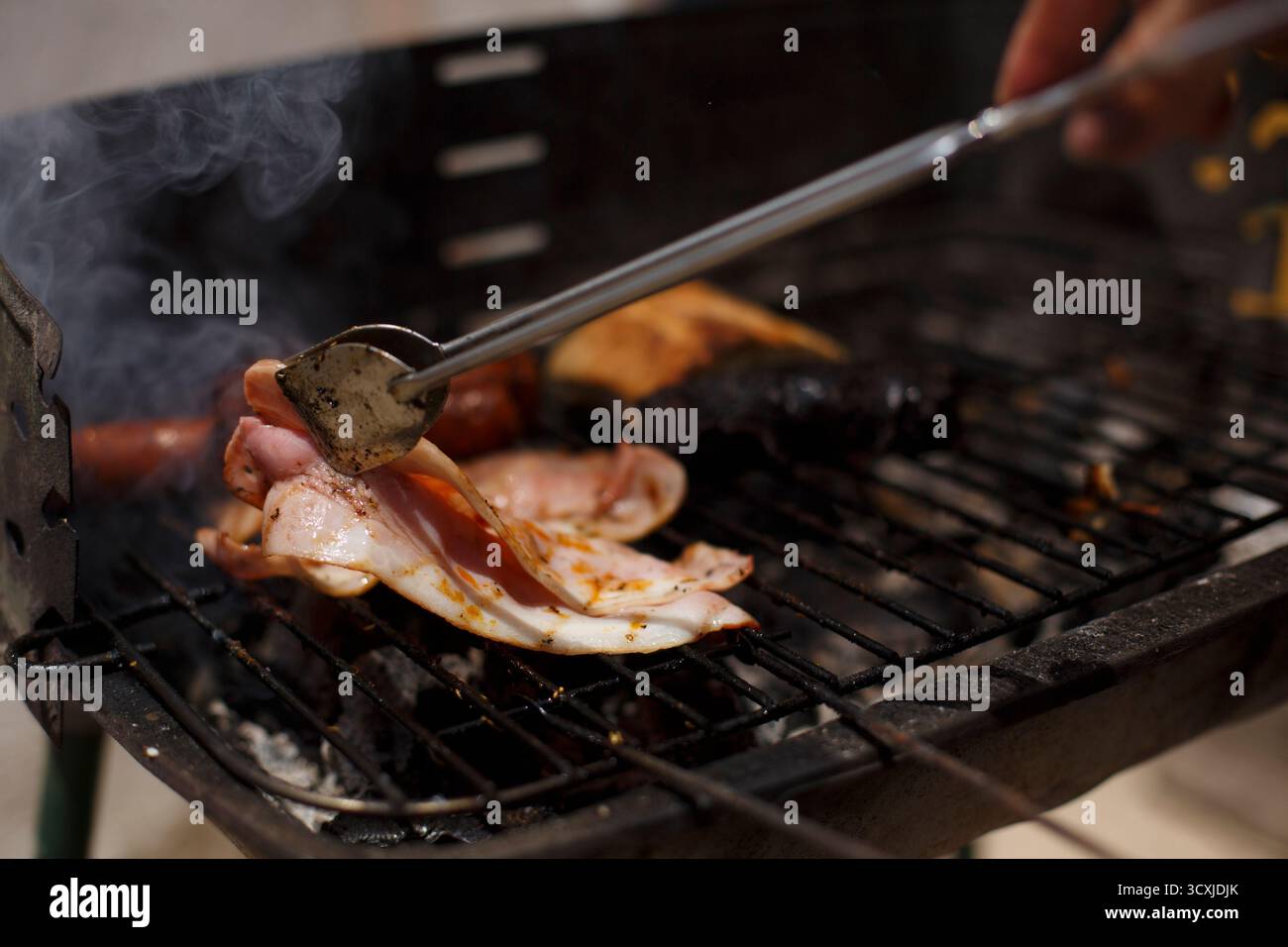 Bacon grésillé et saucisses grillés sur charbon de bois, créant une saveur fumée et parfait pour les barbecues estivaux. Banque D'Images