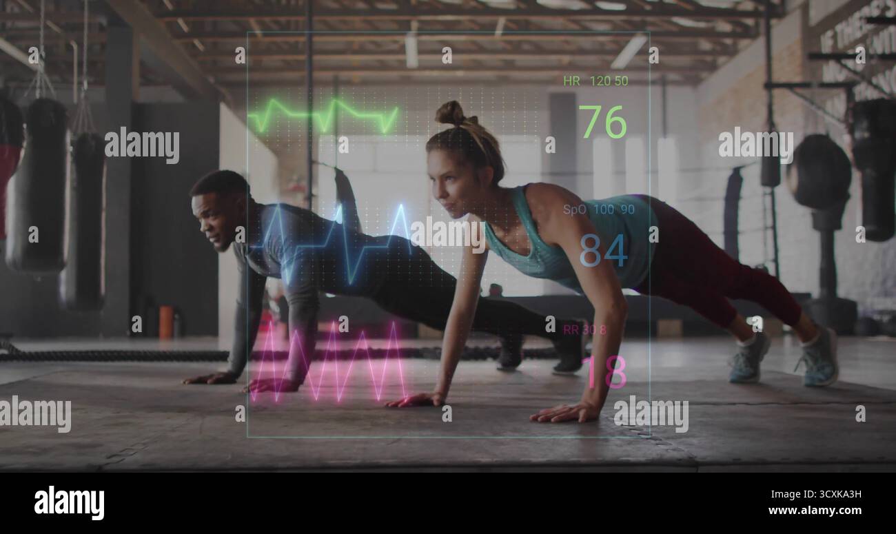 Exécution synchronisée pompes partenaires d'entraînement dans la salle de gym avec sacs de frappe et signes vitaux holographiques Banque D'Images