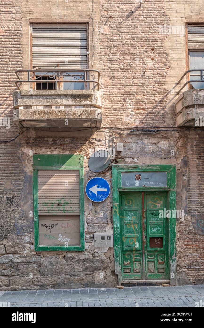 Façade altérée d'un ancien bâtiment avec porte en bois vert, balcons en béton et briques apparentes montrant la décomposition urbaine. Architecture espagnole authentique pour Banque D'Images