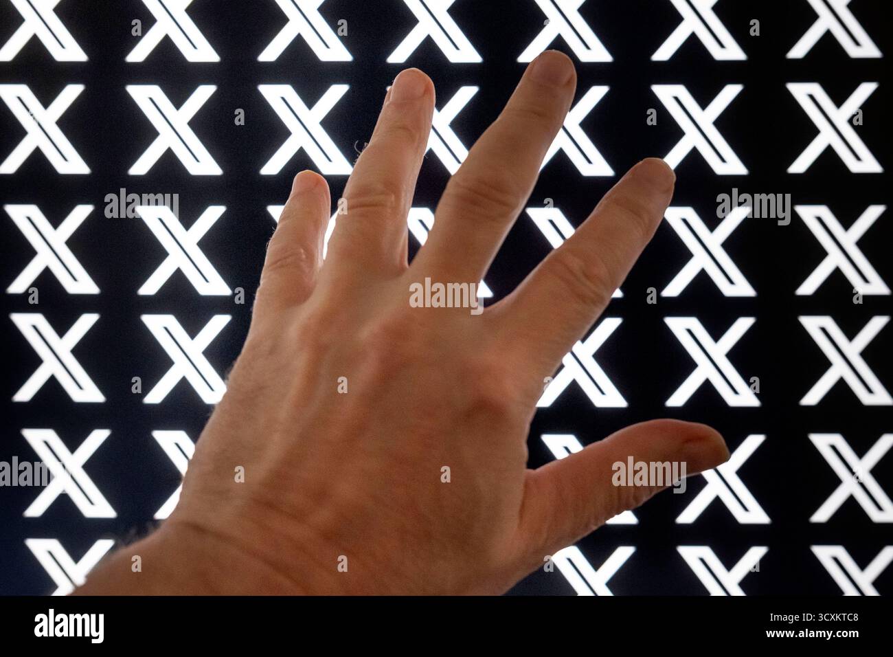 Une main devant un moniteur. En arrière-plan, un écran affiche plusieurs fois le logo de la plateforme X. Image symbolique pour le contenu problématique Banque D'Images