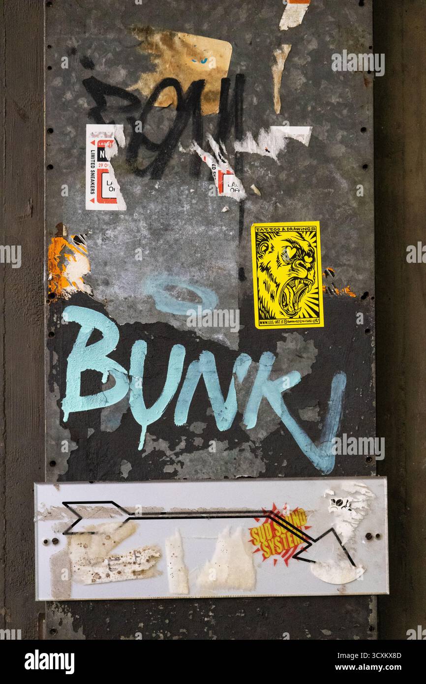 Plaque en métal rouillé recouverte d'autocollants graffiti et d'un symbole de flèche montrant un art de rue authentique dans un environnement urbain. Banque D'Images