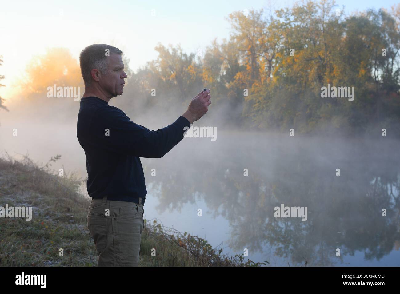 Un homme d'âge moyen prend une photo de téléphone du paysage d'automne le long d'un canal au lever du soleil Banque D'Images Un homme d'âge moyen prend une photo de téléphone du paysage d'automne le long d'un canal au lever du soleil Banque D'Images