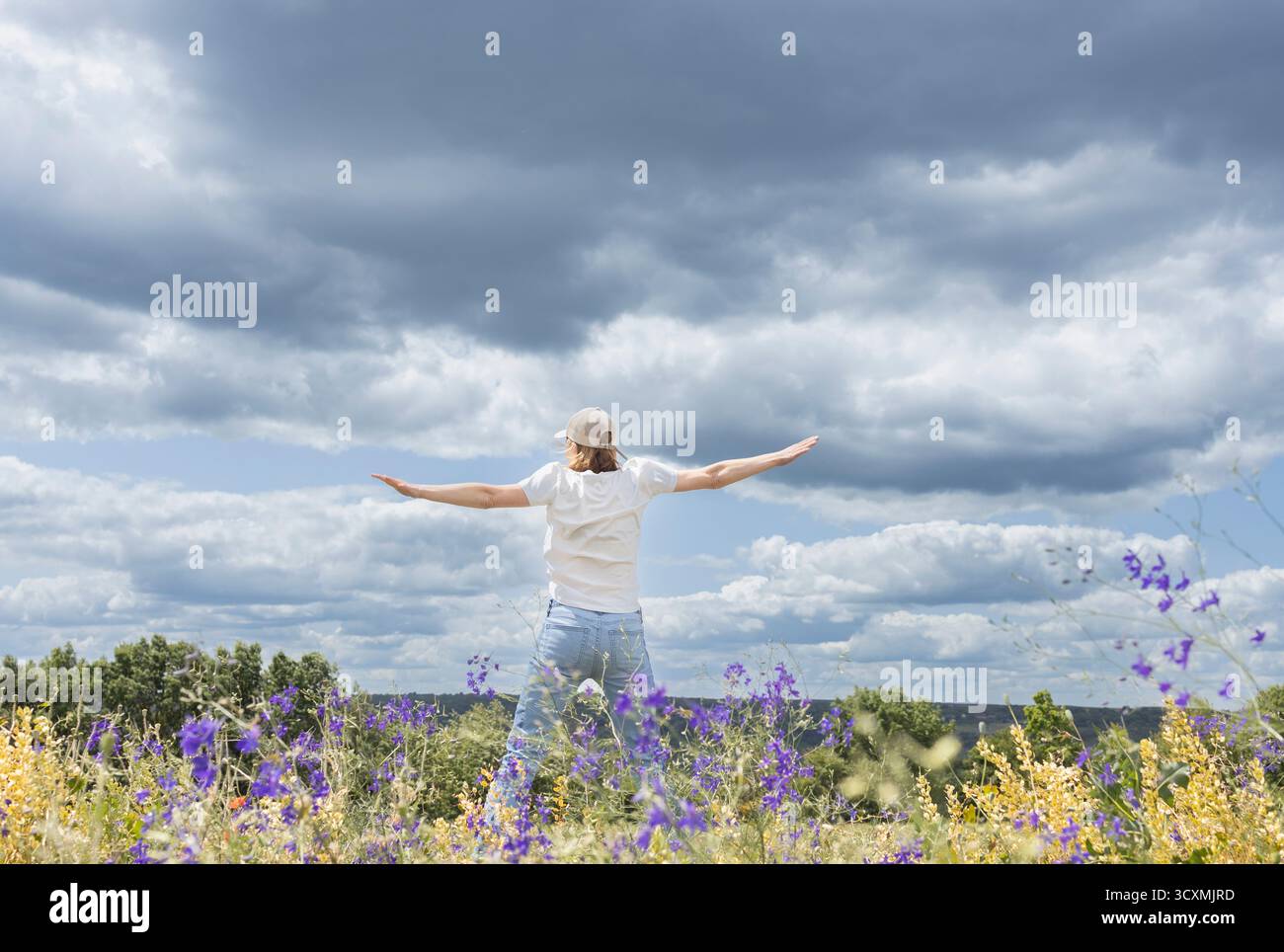 femme se promène dans une prairie fleurie, profitant de la nature. Déployant joyeusement ses bras sur les côtés. Vers un avenir meilleur. Vue arrière. Eart Banque D'Images