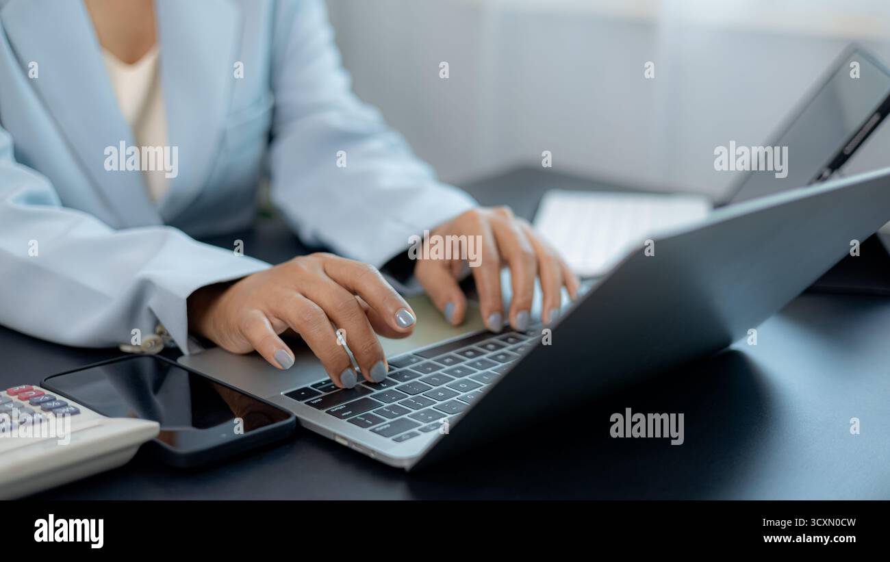 Gros plan de femme d'affaires professionnelle travaillant sur ordinateur portable au bureau avec smartphone et calculatrice, concept de bureau moderne, communication numérique, et Banque D'Images