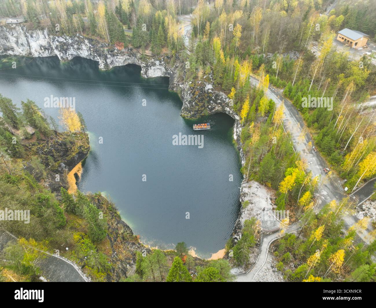 Vue aérienne du lac de carrière de marbre Ruskeala montrant un bateau dans l'eau sombre et des grottes creusées dans les falaises de roche blanche Banque D'Images