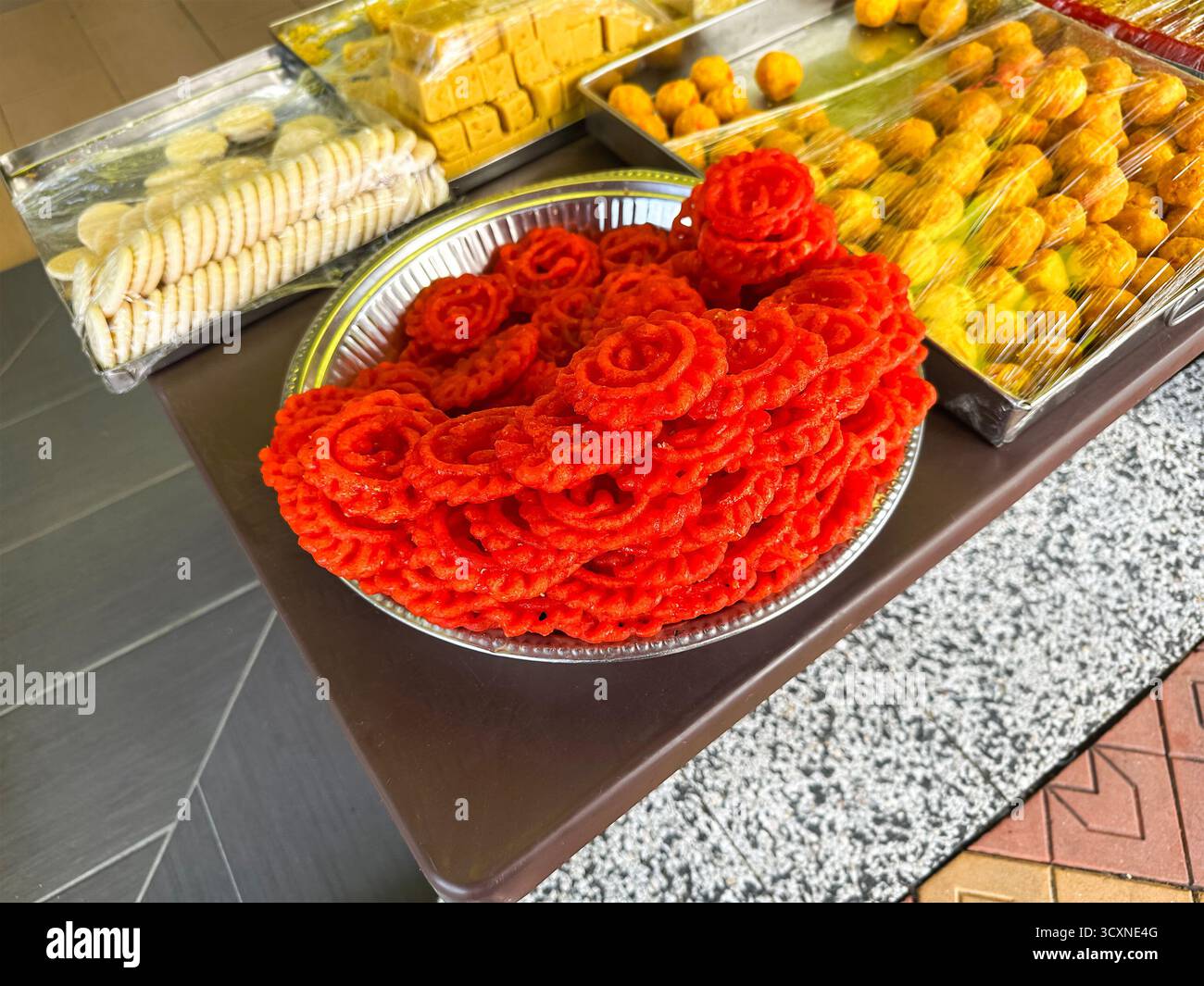 Une table d'exposition de divers bonbons indiens traditionnels, y compris des piles de jalebi rouges à côté de plateaux de délices emballés. Banque D'Images