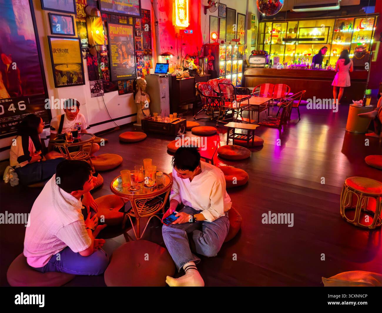 Bar secret caché confortable au thème rétro avec des néons vibrants clients asiatiques dégustant des boissons créant une ambiance chaleureuse kuala lumpur malaysia coussins de sol Banque D'Images
