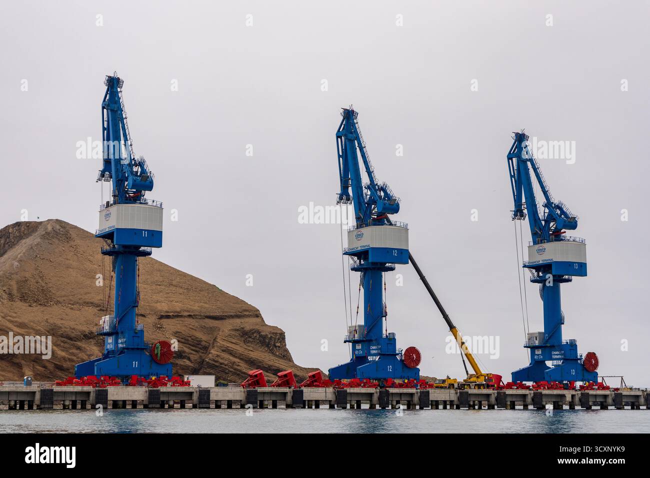 Méga port de Chancay. Trois grues bleues sont sur un quai près d'un plan d'eau. Les grues sont grandes et bleues, et elles sont positionnées dans une rangée. La scène est Banque D'Images Méga port de Chancay. Trois grues bleues sont sur un quai près d'un plan d'eau. Les grues sont grandes et bleues, et elles sont positionnées dans une rangée. La scène est Banque D'Images