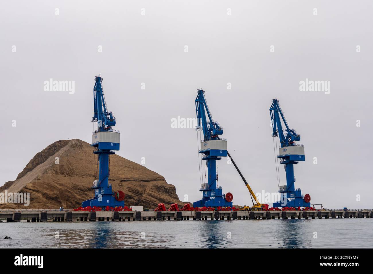 Méga port de Chancay. Trois grues bleues sont sur un quai à côté d'une colline. Les grues sont grandes et bleues, et elles sont positionnées dans une rangée. La scène est calme Banque D'Images Méga port de Chancay. Trois grues bleues sont sur un quai à côté d'une colline. Les grues sont grandes et bleues, et elles sont positionnées dans une rangée. La scène est calme Banque D'Images
