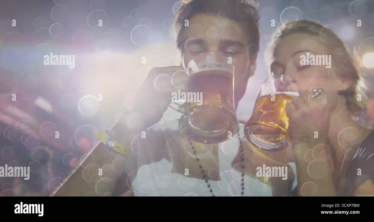 Soulever l'homme et la femme buvant de grandes tasses de bière en verre à la tente du festival, avec des lumières bokeh Banque D'Images