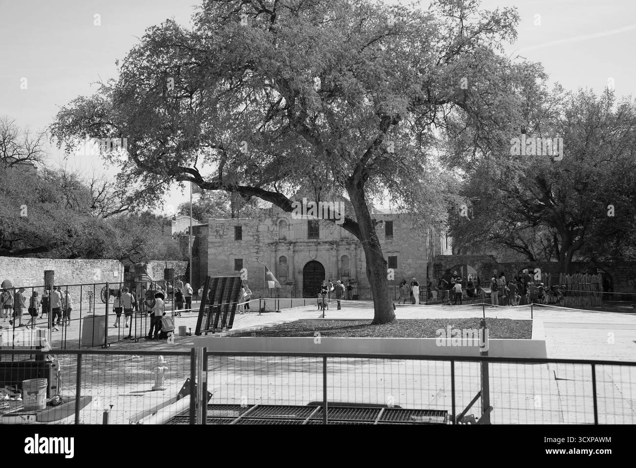 Image en noir et blanc de la mission Alamo entourée d'une clôture pendant les travaux de préservation, avec des visiteurs explorant le monument historique Banque D'Images