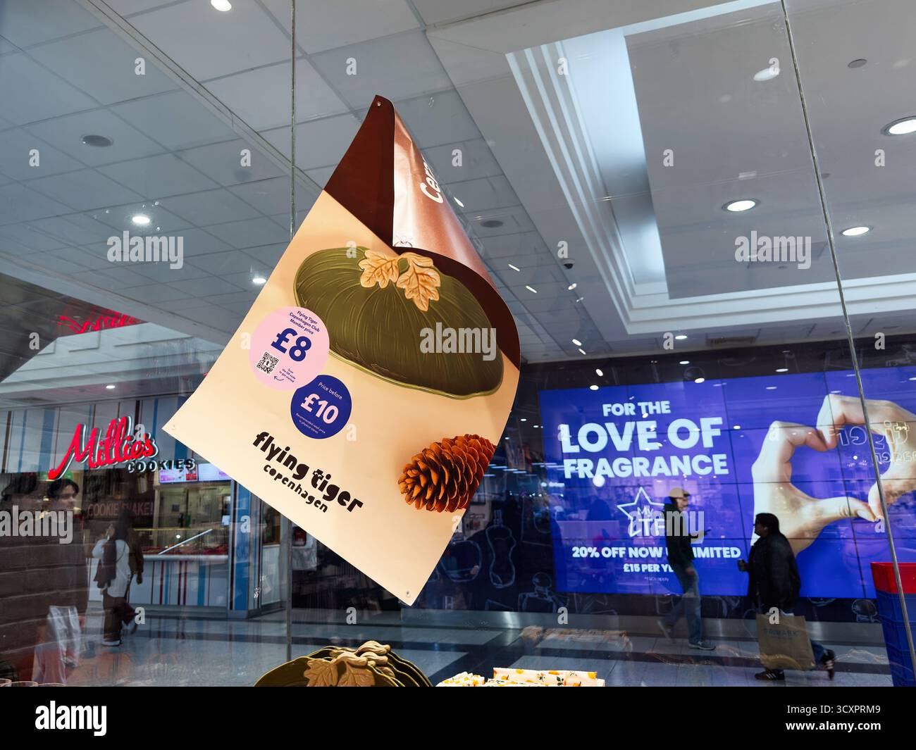 Manchester, Royaume-Uni - 26 septembre 2025 : une grande affiche suspendue dans un centre commercial moderne avec une boutique de biscuits Flying Tiger Copenhagen visible et un avver de parfum Banque D'Images
