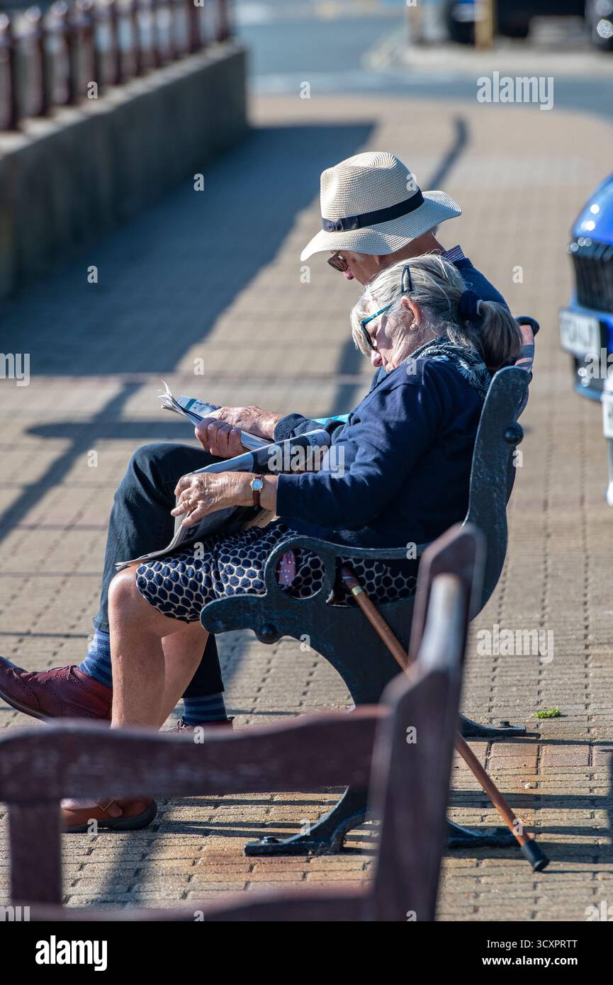 couple plus âgé profitant d'un après-midi de détente assis sur un banc au bord de la mer par une journée ensoleillée, dame âgée s'endormant sur l'épaule des maris au soleil. Banque D'Images